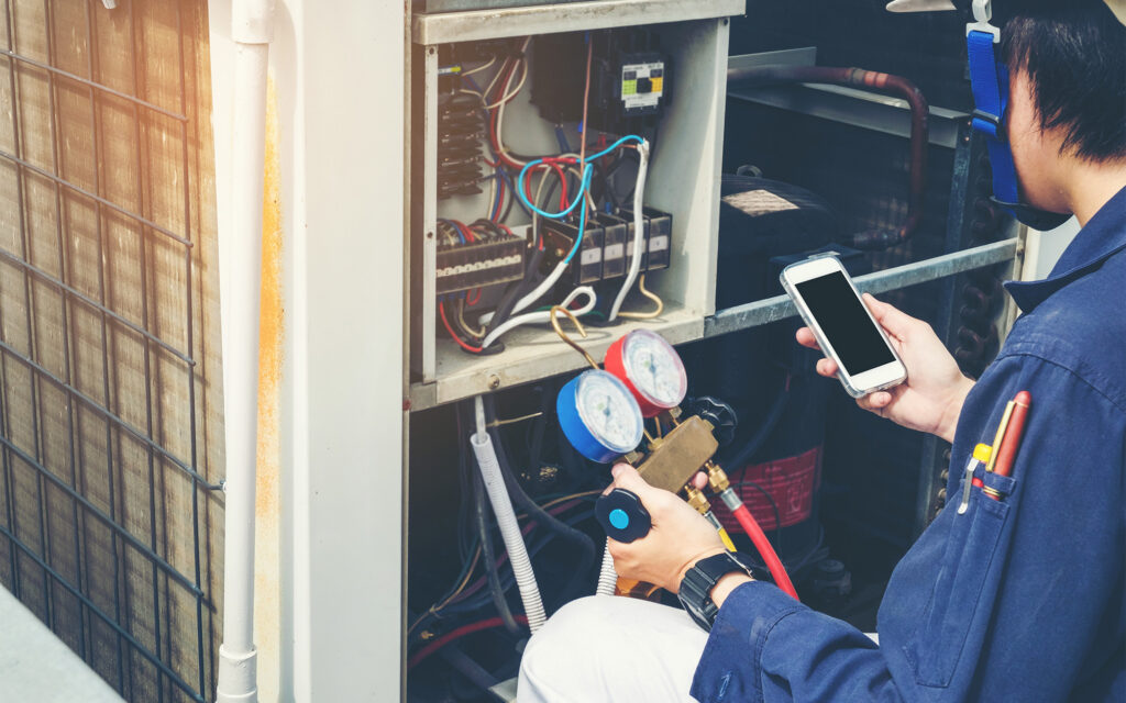 HVAC technician looking at data on phone and holding guage next to roof unit